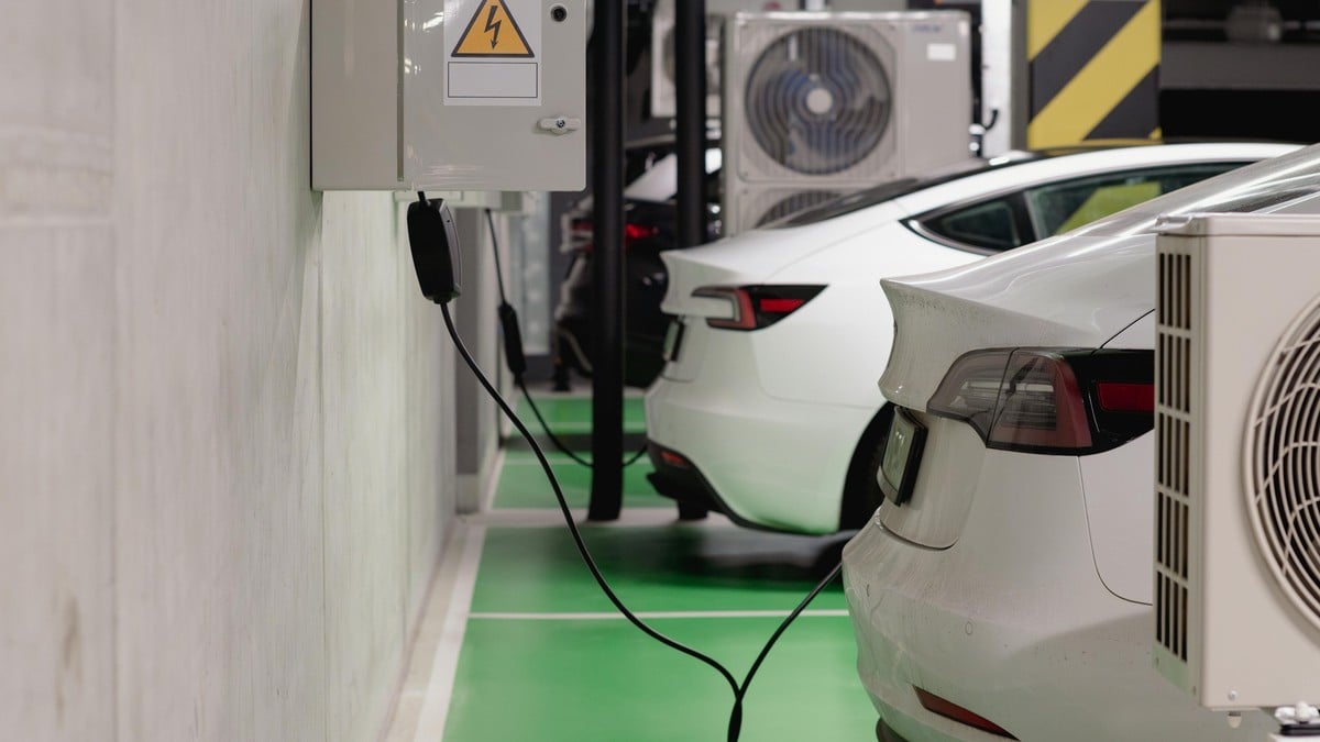 Two white 2026 Tesla Model S vehicles are parked in a garage, with one connected to a charging station on the wall.