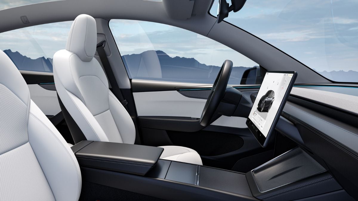 White leather interior of Tesla Model Y with large touchscreen, mountain landscape visible through open door, minimalist design with black and white color scheme