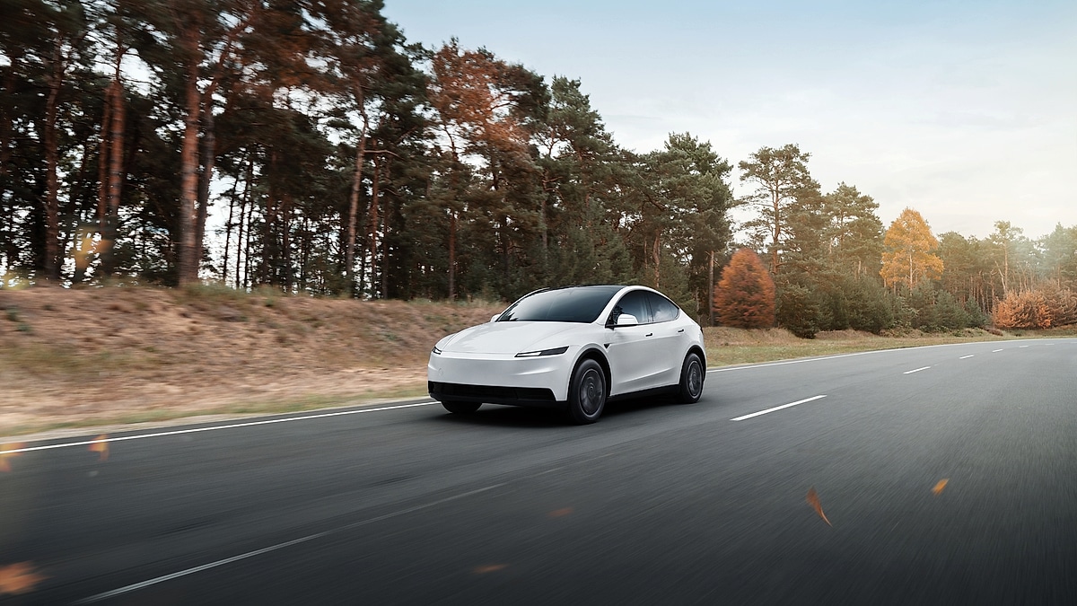 Tesla Model Y electric SUV driving on a highway with autumn trees