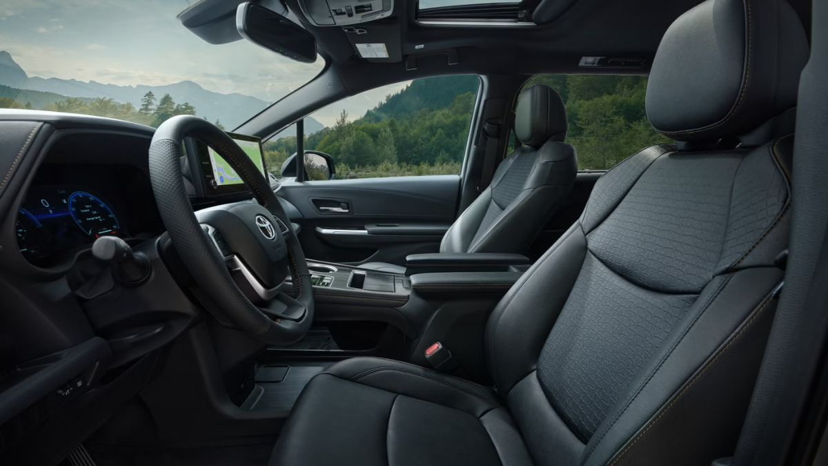 Interior view of a 2025 Toyota Sienna showing premium black upholstered seats with quilted pattern stitching, modern dashboard with digital displays, and scenic mountain views visible through the windows.