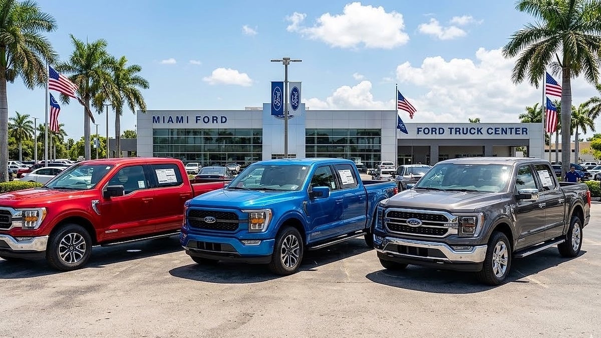 Three new Ford F-150 trucks—red, blue, and gray models—on a sunny Miami dealership lot with palm trees