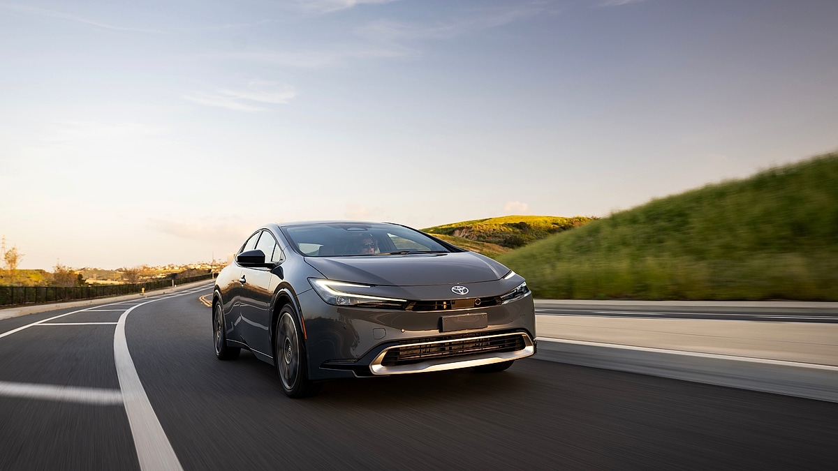 Toyota Prius Prime driving on road at sunset with hills in background