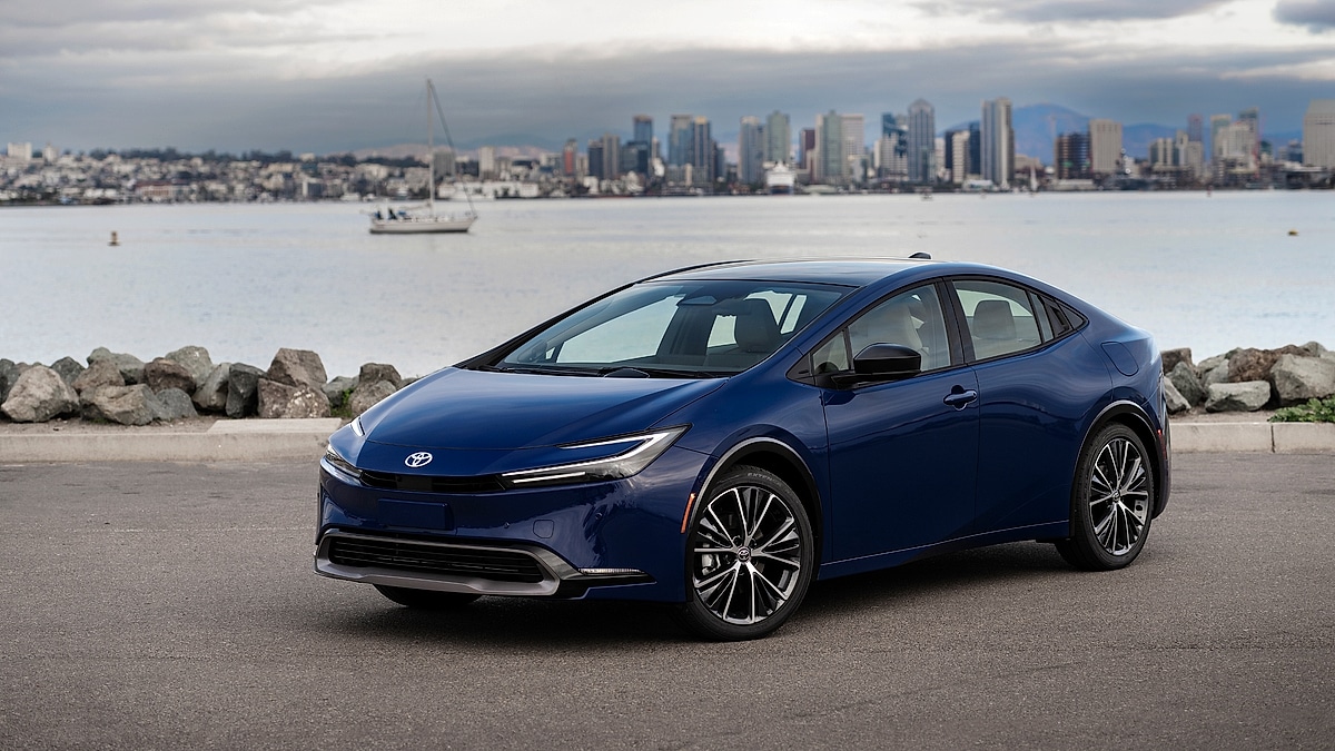 Blue Toyota Prius parked near waterfront with city skyline in background