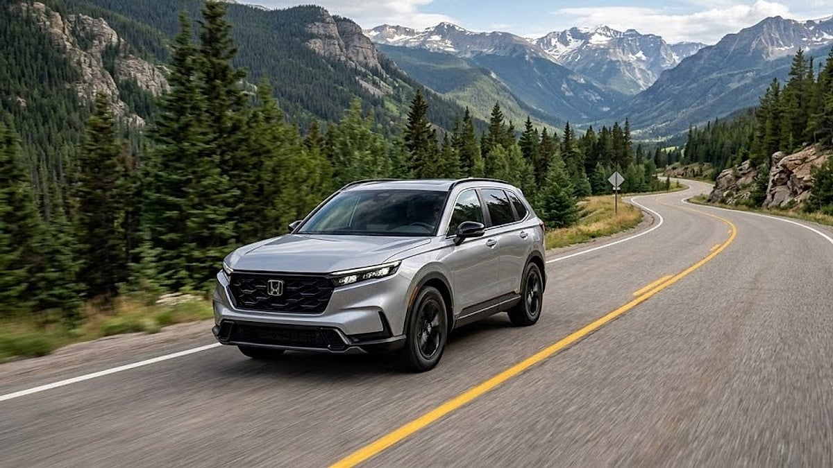 A 2023 Honda CR-V travels along a winding two-lane mountain highway surrounded by evergreen forests and rugged peaks