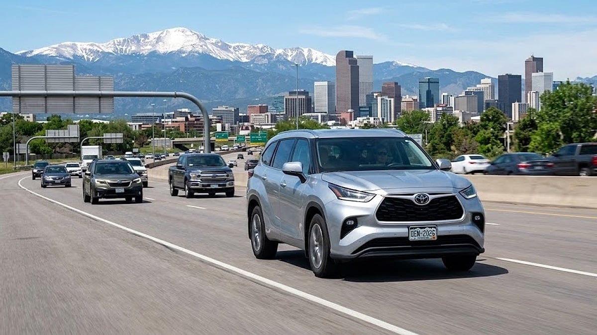 A 2023 Silver Toyota Highlander driving on Denver highway with Rocky Mountains and skyline