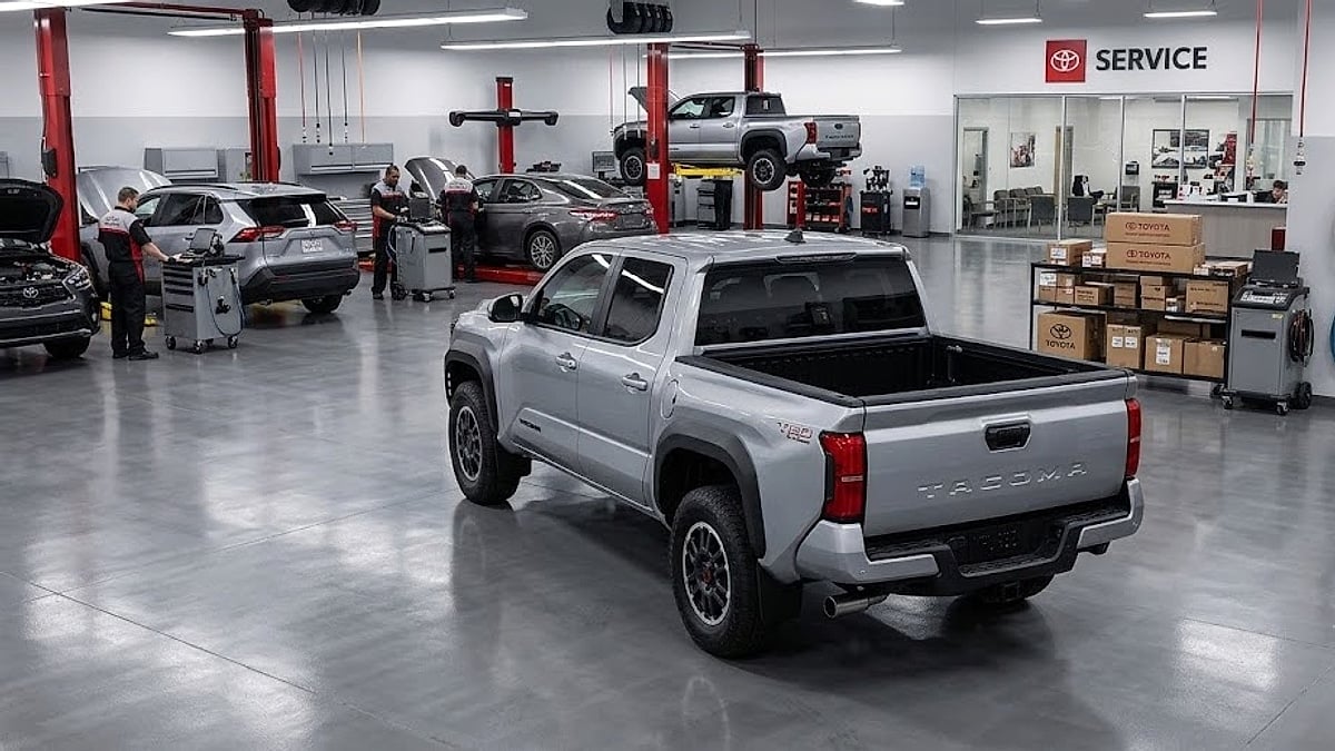 A 2024 Toyota Tacoma sits reversed inside a busy dealership service bay, showcasing its rear cab design and cargo bed
