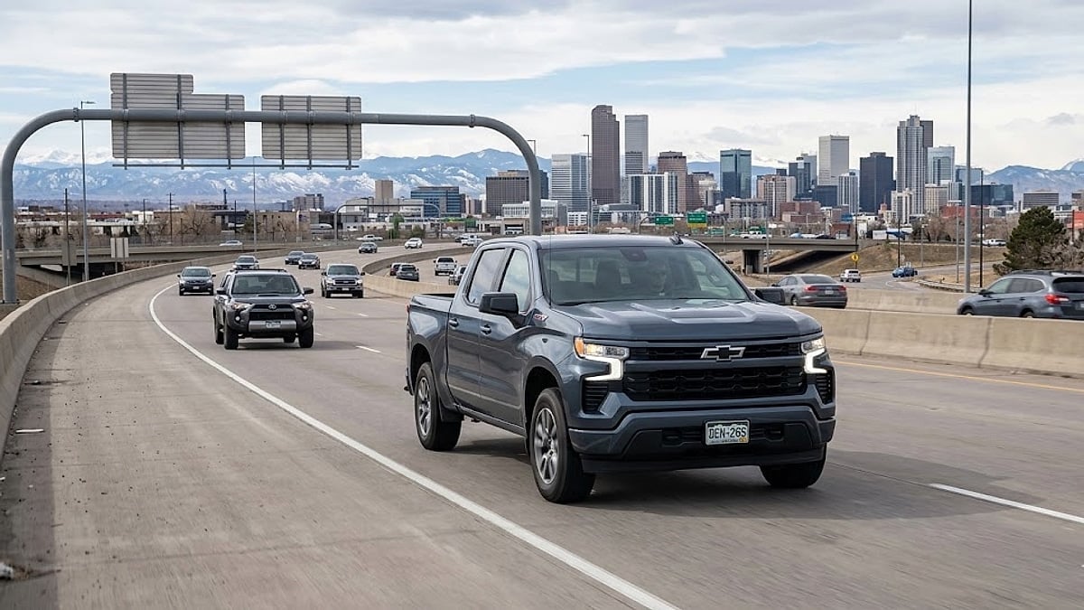A 2026 Chevy Silverado RST with Colorado plates drives on a Denver highway towards the downtown skyline and mountains