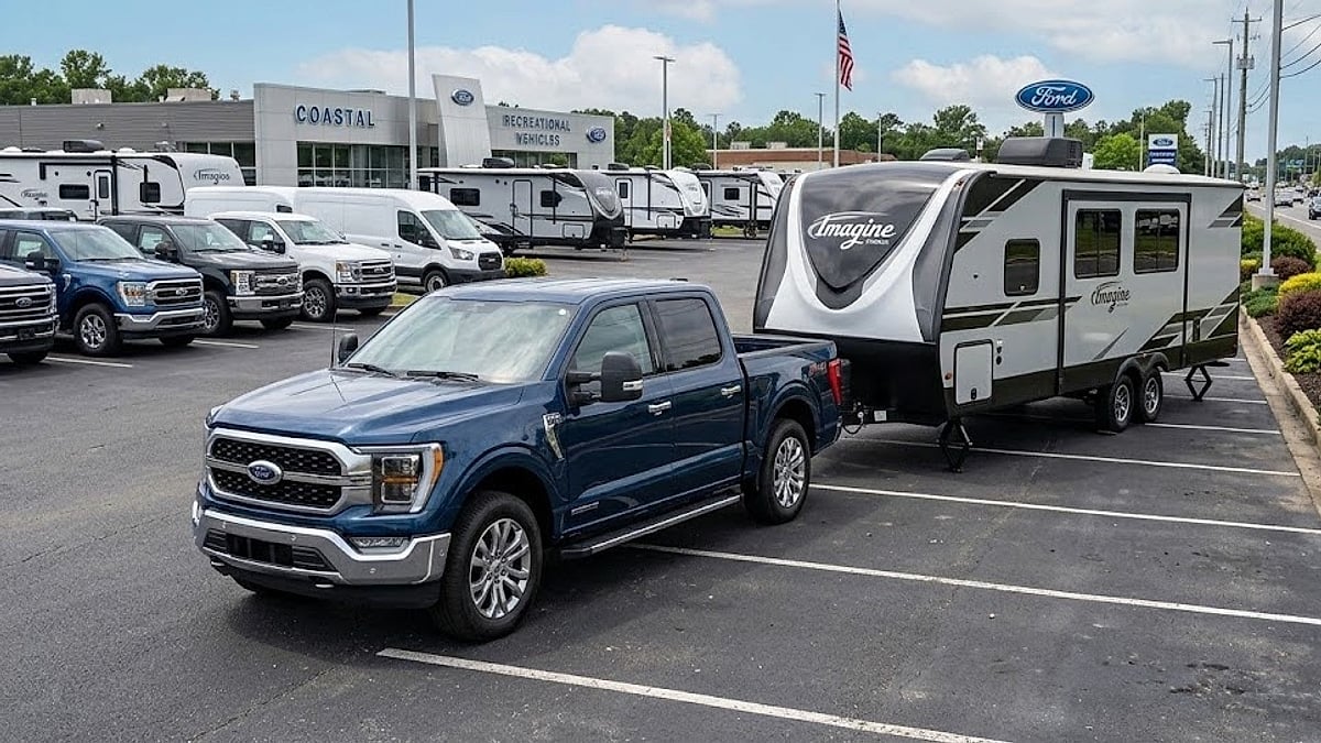 A blue 2026 Ford F-150 secures a large Grand Design Imagine camper trailer at a dealership lot before summer travels