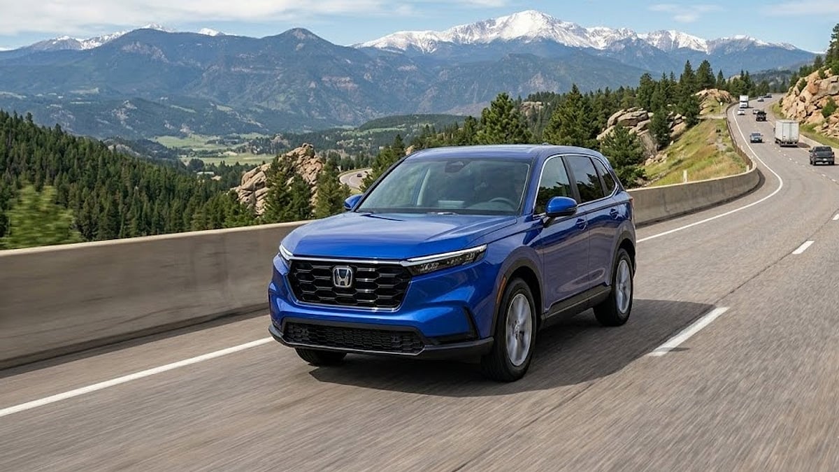 A blue 2026 Honda CR-V Hybrid drives along a mountain highway curve, showcasing its dynamic performance on Floyd Hill