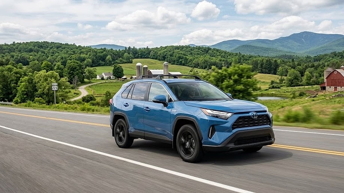 A new 2026 Toyota RAV4 Hybrid driving on a winding Vermont highway with green hills and mountains in background