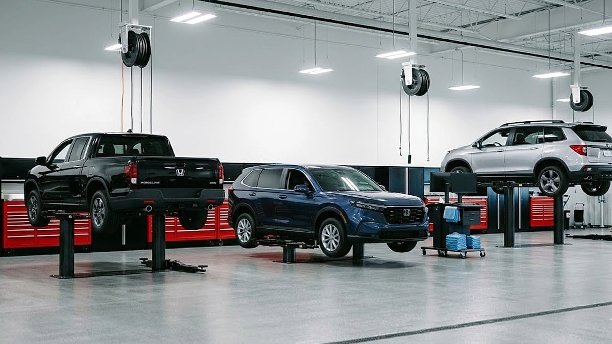 A clean, professional Honda service bay with a blue CR-V, silver SUV, and black truck, elevated on hydraulic lifts