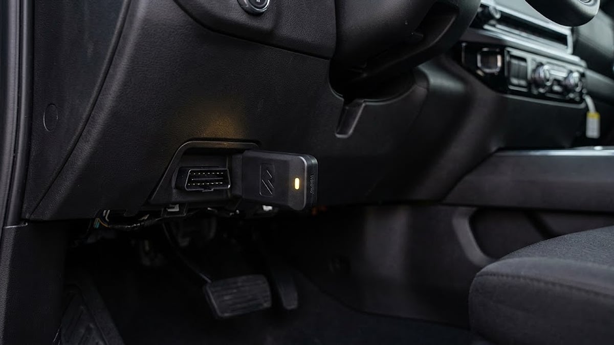 A close-up of a Range Technology DFM Disabler module with an amber LED light plugged into a Chevy Silverado OBD-II port