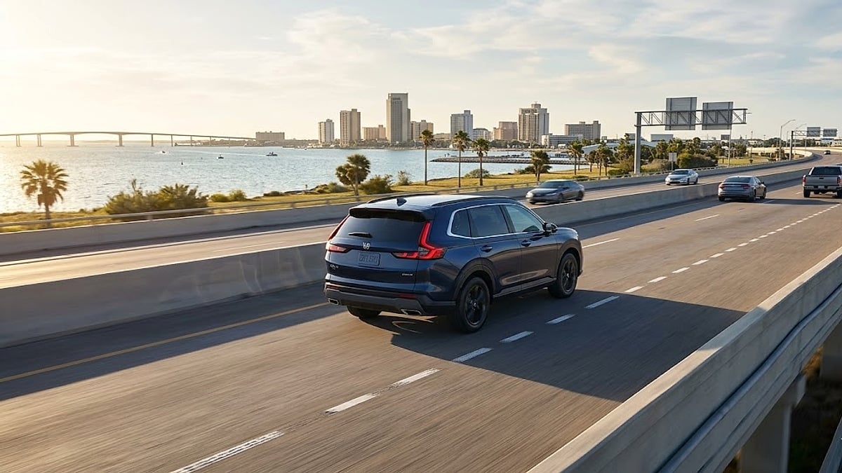 A close-up photograph capturing a clean, dark-blue 2025 Honda CR-V Hybrid driving on a multi-lane elevated highway in Corpus Christi, Texas