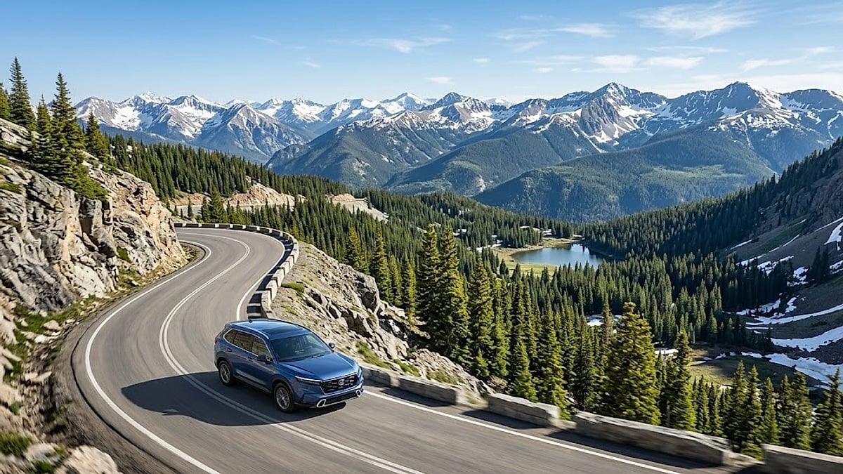 A dark-blue 2026 Honda CR-V driving on a winding Colorado mountain road with snow-capped peaks and evergreen forests