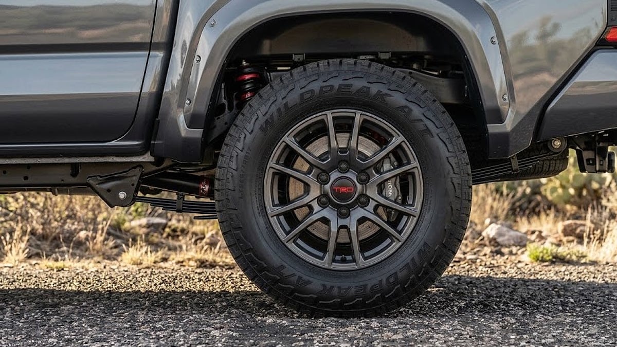A detailed close-up of a dark multi-spoke wheel on a gray 2026 Toyota Tacoma TRD, highlighting aggressive multi-terrain tire tread-optimized