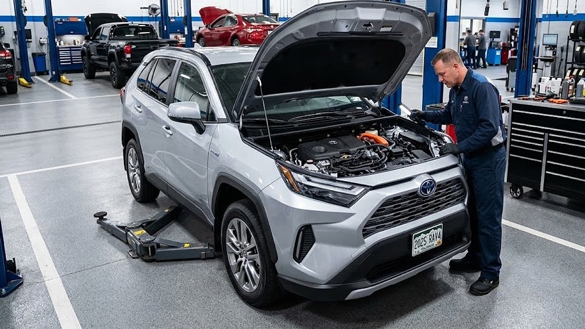 A mechanic inspects the open engine bay of a silver 2025 Toyota RAV4 using a flashlight inside a service bay