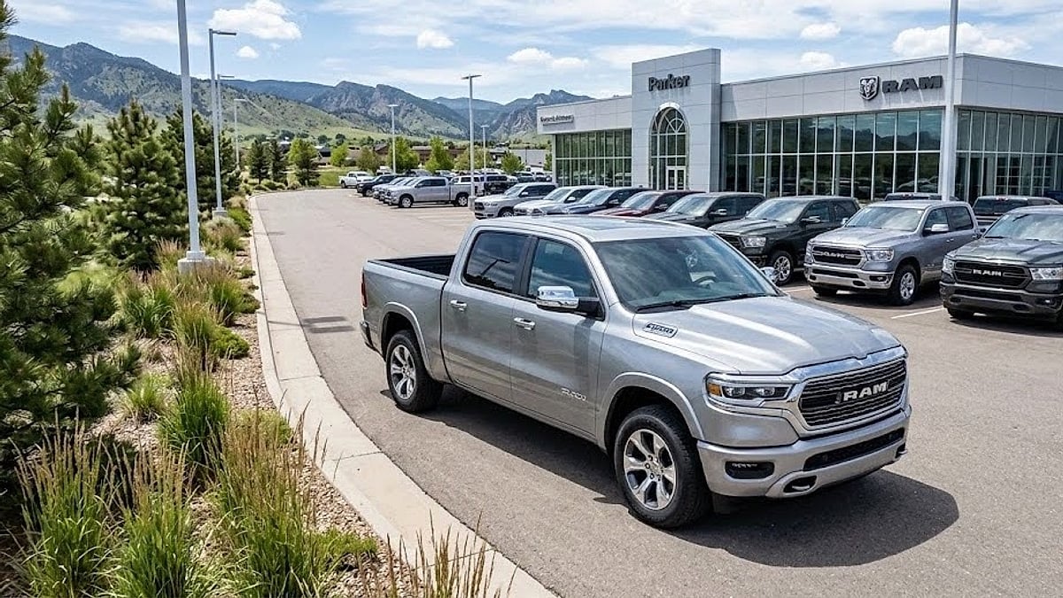 A new silver 2026 Ram pickup stands parked in the foreground of a modern commercial vehicle dealership lot on a clear day
