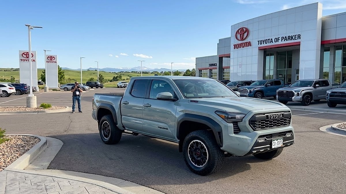 A pristine 2025 Toyota Tacoma sits on a dealership lot, showcasing its rugged front grille and redesigned midsize stance