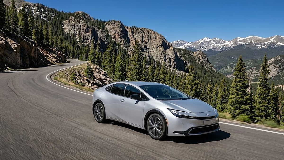 A silver 2025 Toyota Prius driving dynamically on a paved, winding mountain pass through the Colorado Rockies on a clear