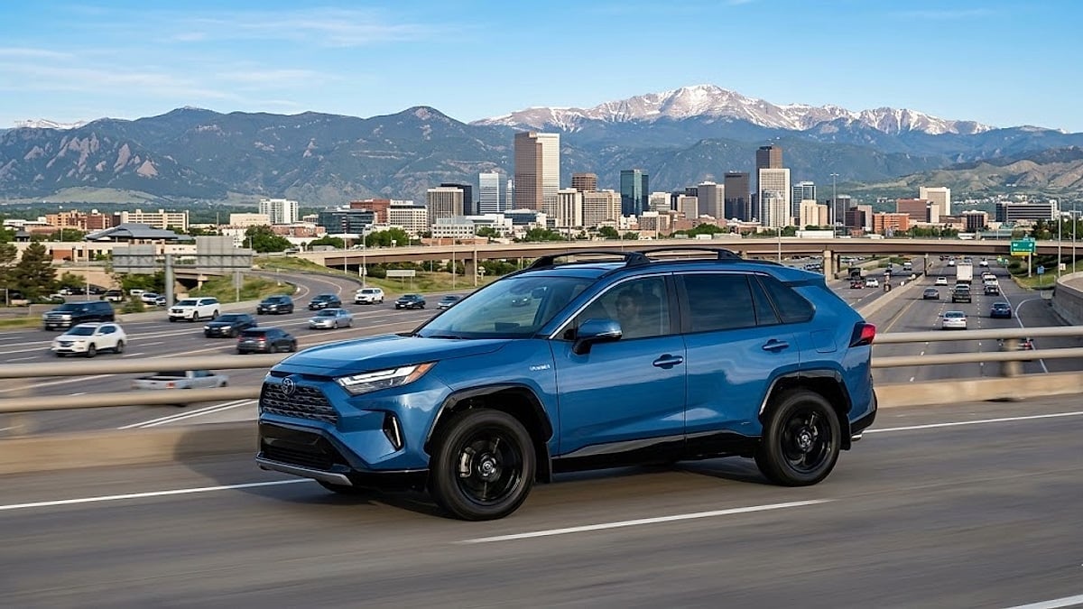 A silver Toyota RAV4 with passengers navigates a Denver, Colorado highway framed by the Rocky Mountains