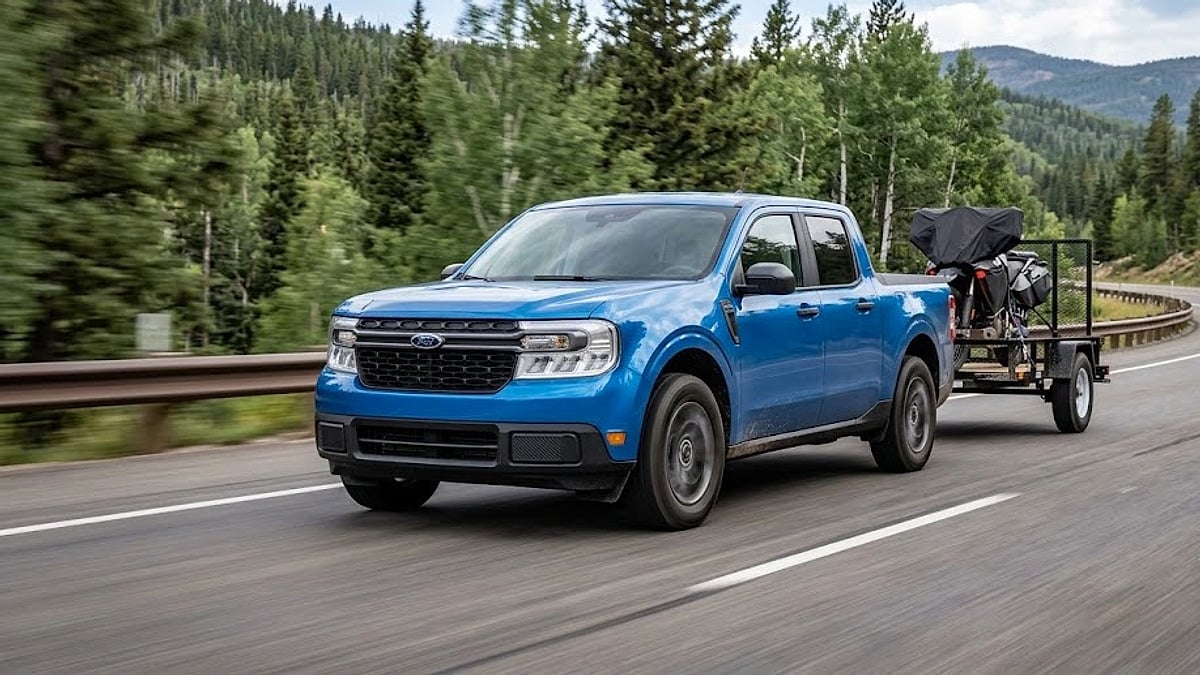 A Velocity Blue 2026 Ford Maverick Hybrid towing a utility load on a mountain highway