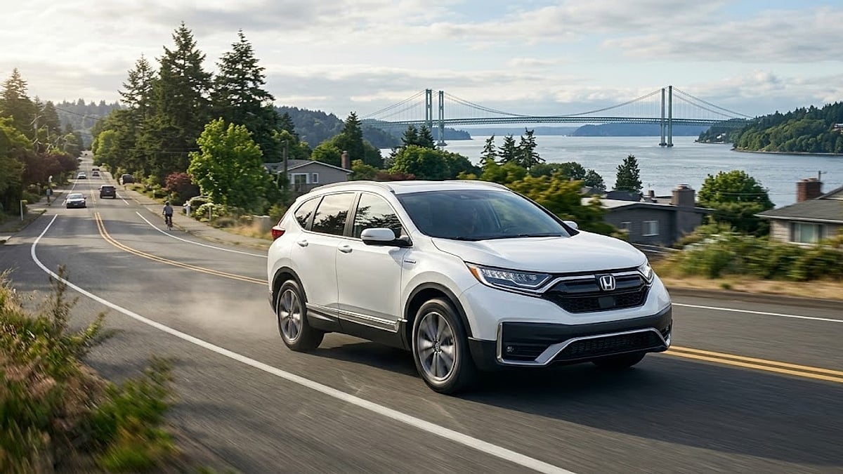A white 2020 Honda CR-V Hybrid travels along a coastal highway road with the Tacoma Narrows Bridge visible behind it