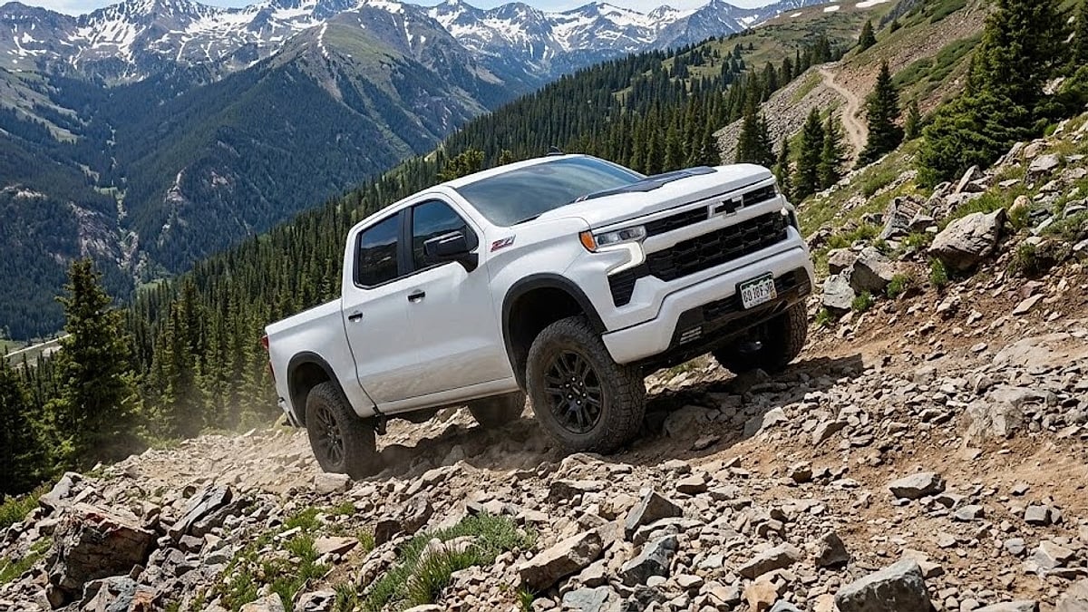 A white 2026 Chevy Silverado negotiates a rugged Colorado off-road mountain grade with majestic, snow-capped peaks in the background