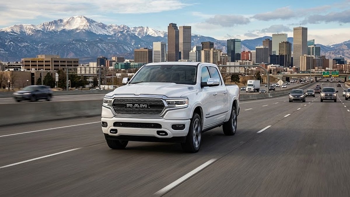A white 2026 Ram 1500 truck drives on a Denver highway with the Colorado Rocky Mountain skyline in the background