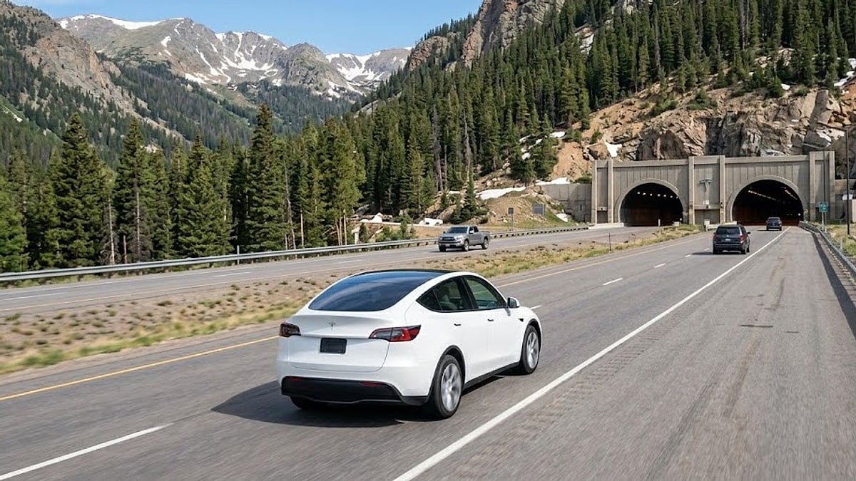 A white Tesla Model Y climbs Interstate 70 toward the Eisenhower Tunnel, testing its heavy chassis components under severe mountain grades