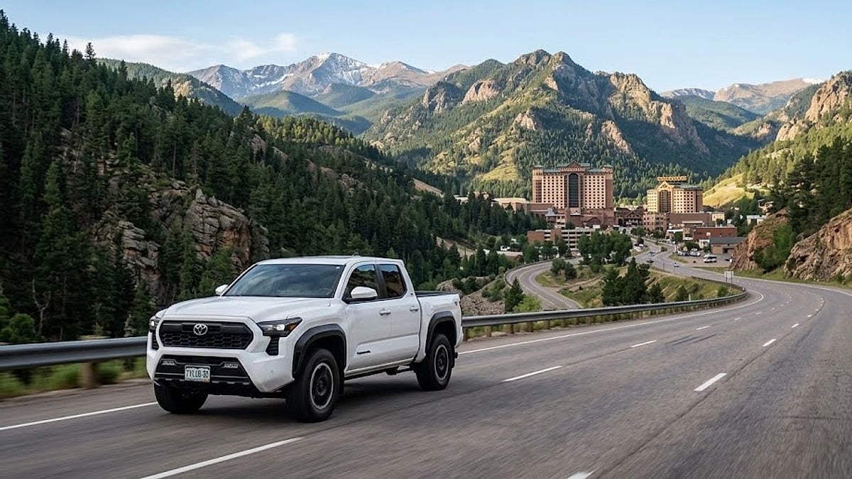 A white Toyota Tacoma TRD Off-Road drives along a scenic Colorado mountain highway approaching the Black Hawk valley and casino resorts