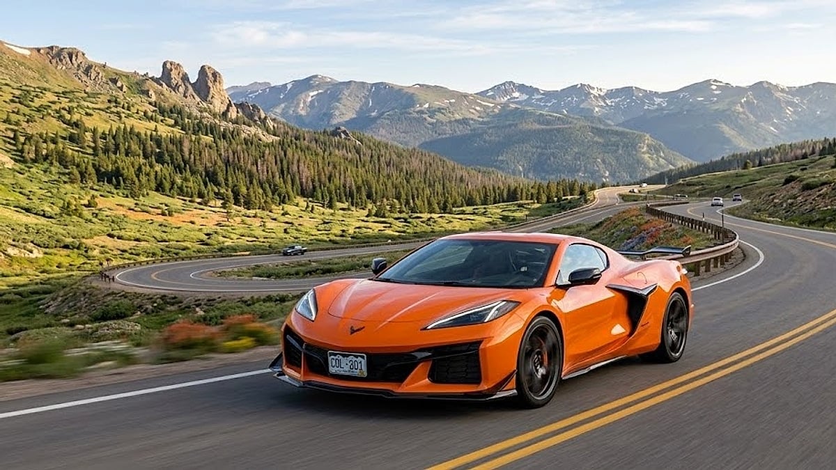 An orange Chevrolet Corvette C8 ZR1 drives dynamically along a winding high-altitude mountain pass road with panoramic Rocky Mountain views