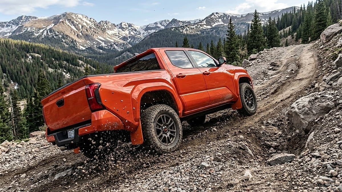 An orange Toyota Tacoma TRD Pro powers up a steep, gravel-covered Colorado mountain trail, demonstrating high-clearance off-road capability