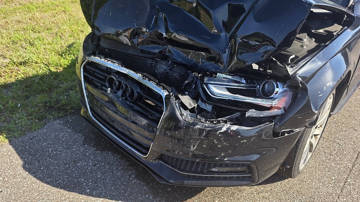 Close-up of the damaged front corner of an Audi A4 showing a crumpled hood, broken grille, and headlight damage.
