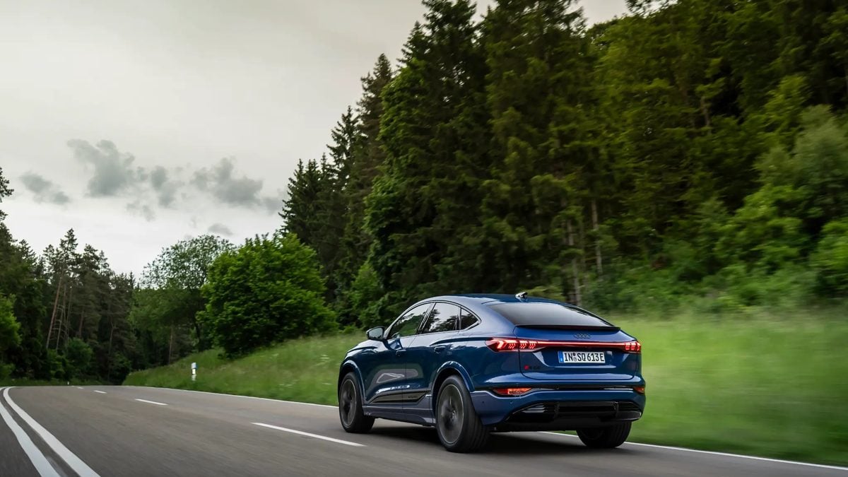Blue Audi Q4 e-tron electric SUV driving on a winding forest highway in motion
