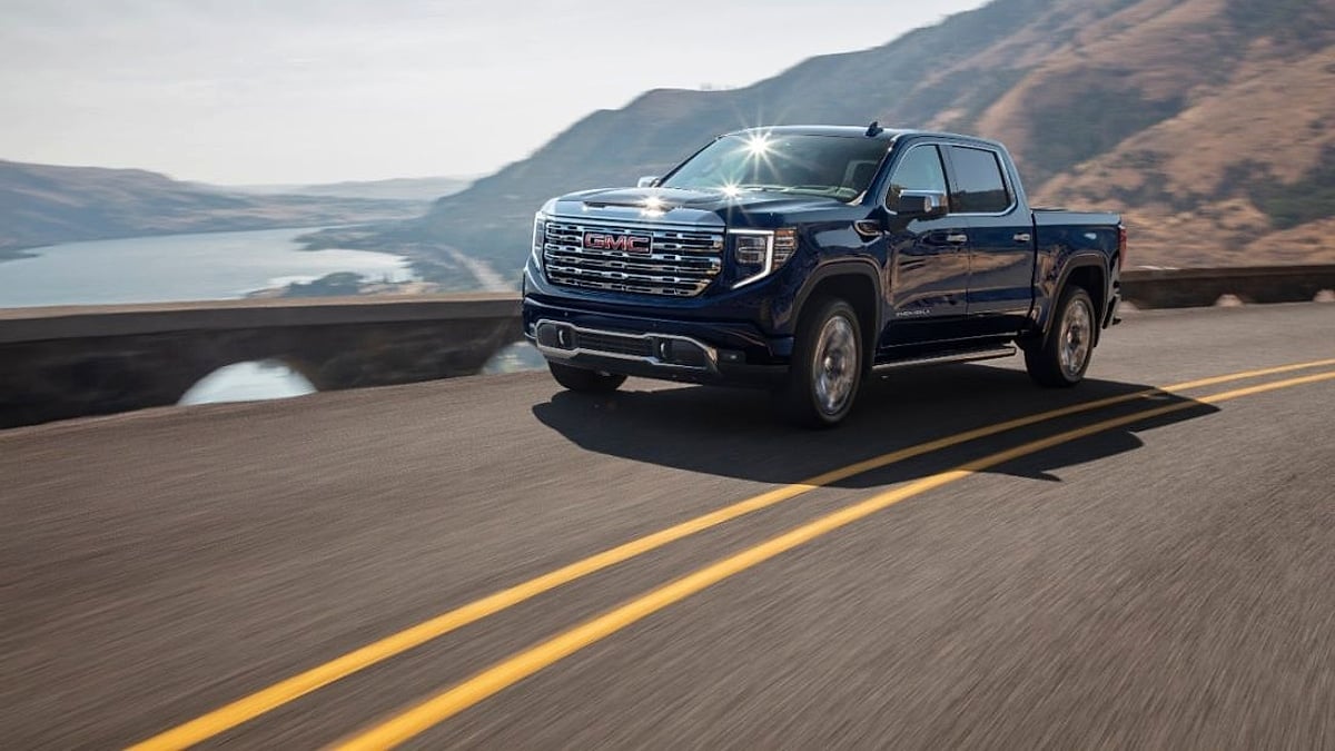 Blue GMC Sierra 1500 pickup truck driving on a mountain road above a river canyon.