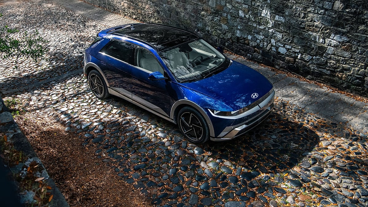 Blue Hyundai Ioniq 5 shown from above on a cobblestone street beside a stone wall.