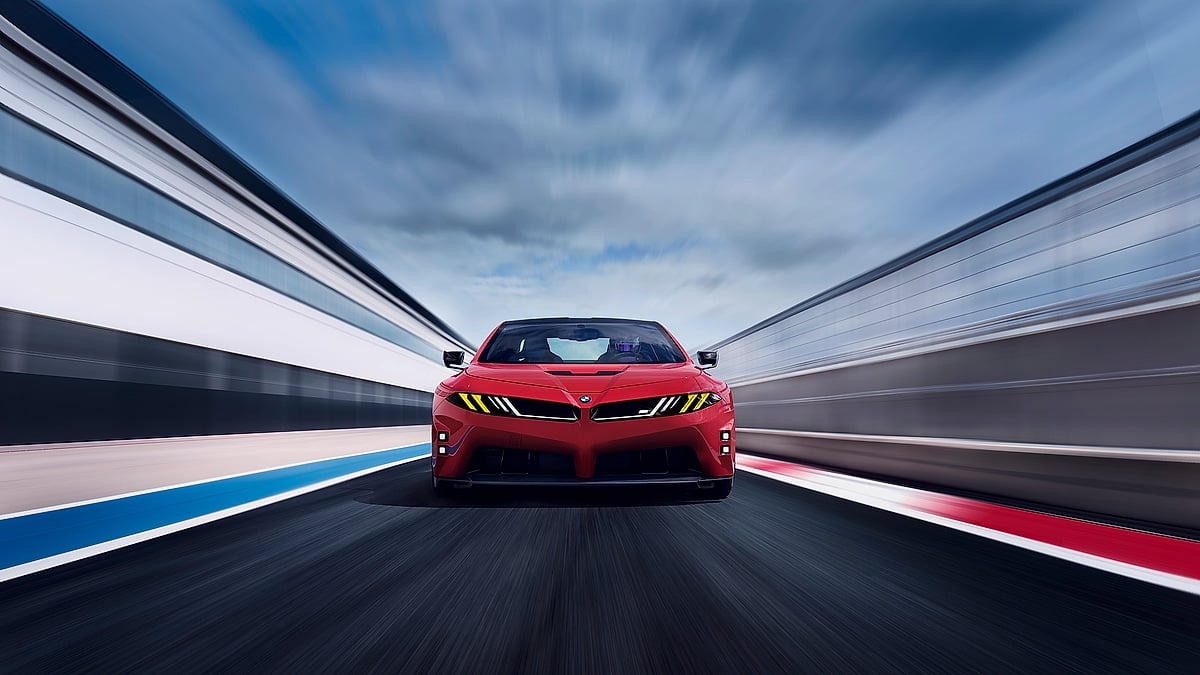 Red BMW M concept car driving head-on down a racetrack with motion blur and dramatic clouds.