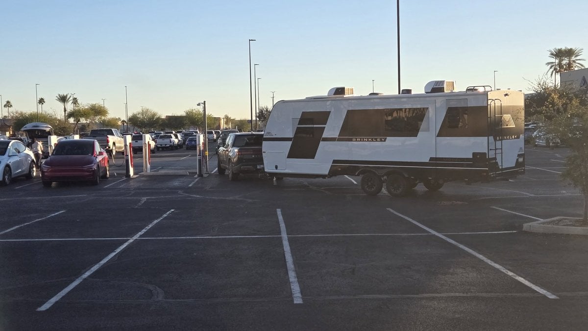 White Brinkley RV trailer parked in sunny lot with palm trees and vehicles