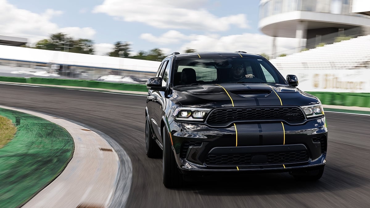 Black Dodge Durango Alchemi with yellow stripes driving on a racetrack in a front action view.