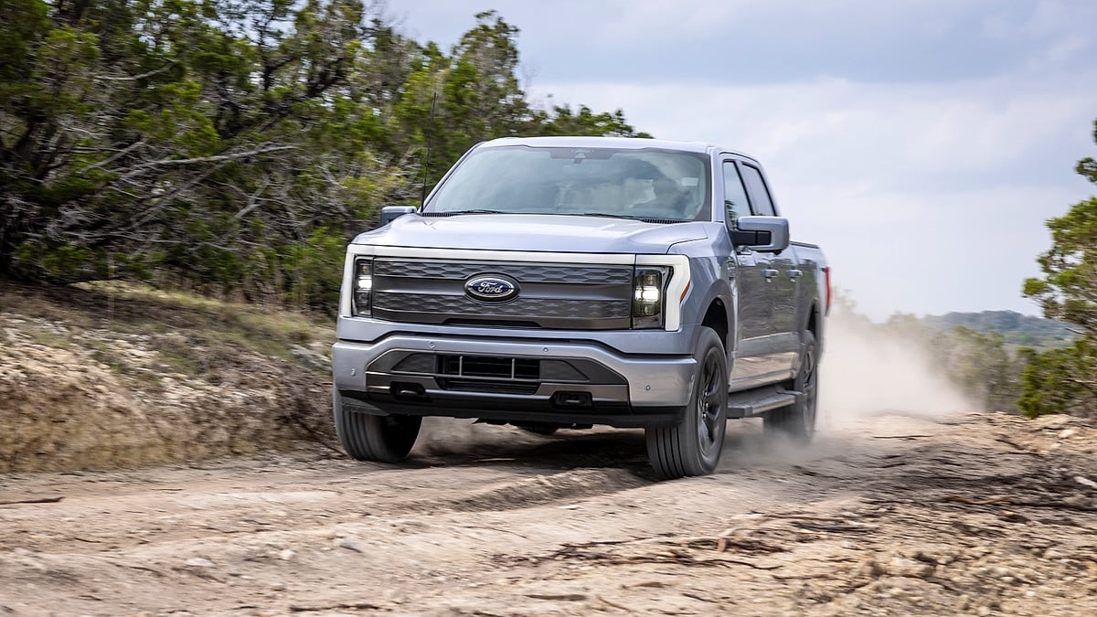 Ford F-150 Lightning Lariat driving on a dirt trail through the woods, kicking up dust from the front tires.