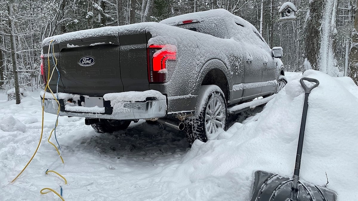 Ford F-150 PowerBoost covered in snow with power cords hanging from the tailgate during a winter storm.