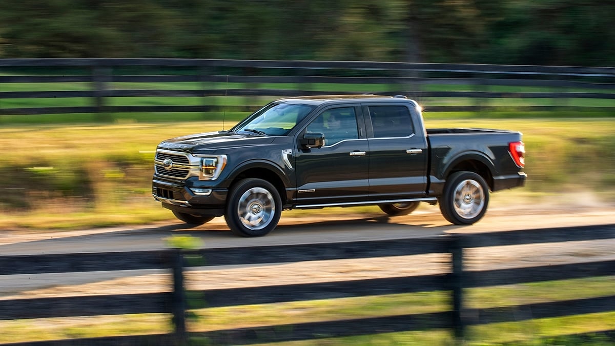 Red Ford F-150 pickup driving along a tree-lined road with motion blur in the surrounding forest.