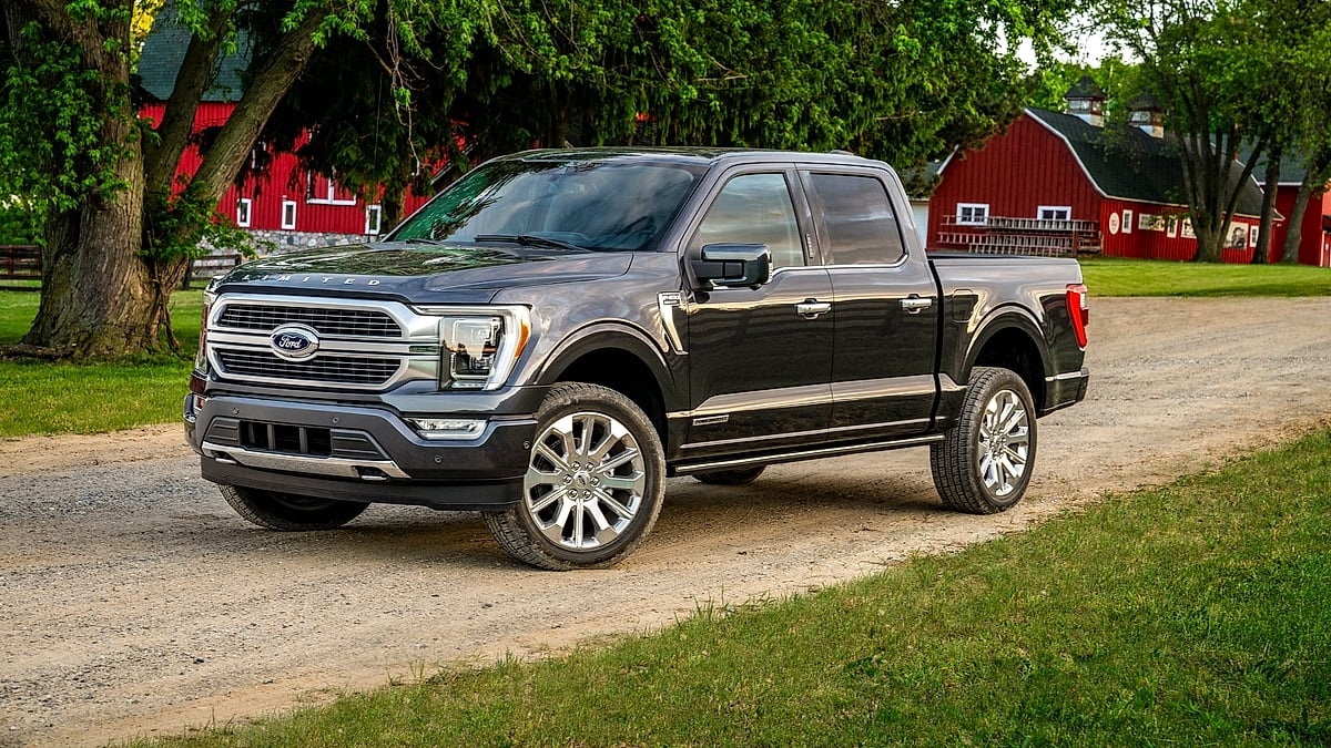 Gray Ford F-150 pickup parked on a gravel driveway near red barns and green trees at a farm.