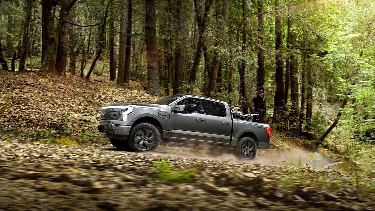 Ford F-150 Lightning electric pickup truck driving on a dirt forest trail.