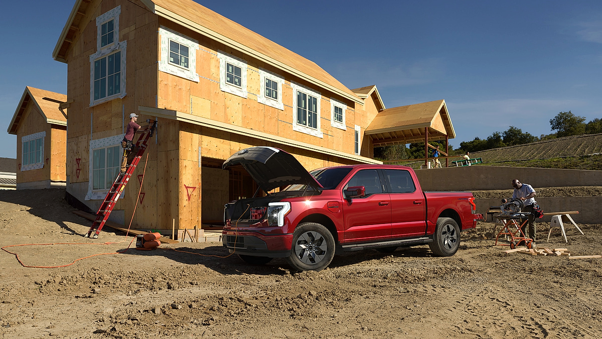 Red Ford F-150 Lightning electric pickup powering tools at a home construction site.