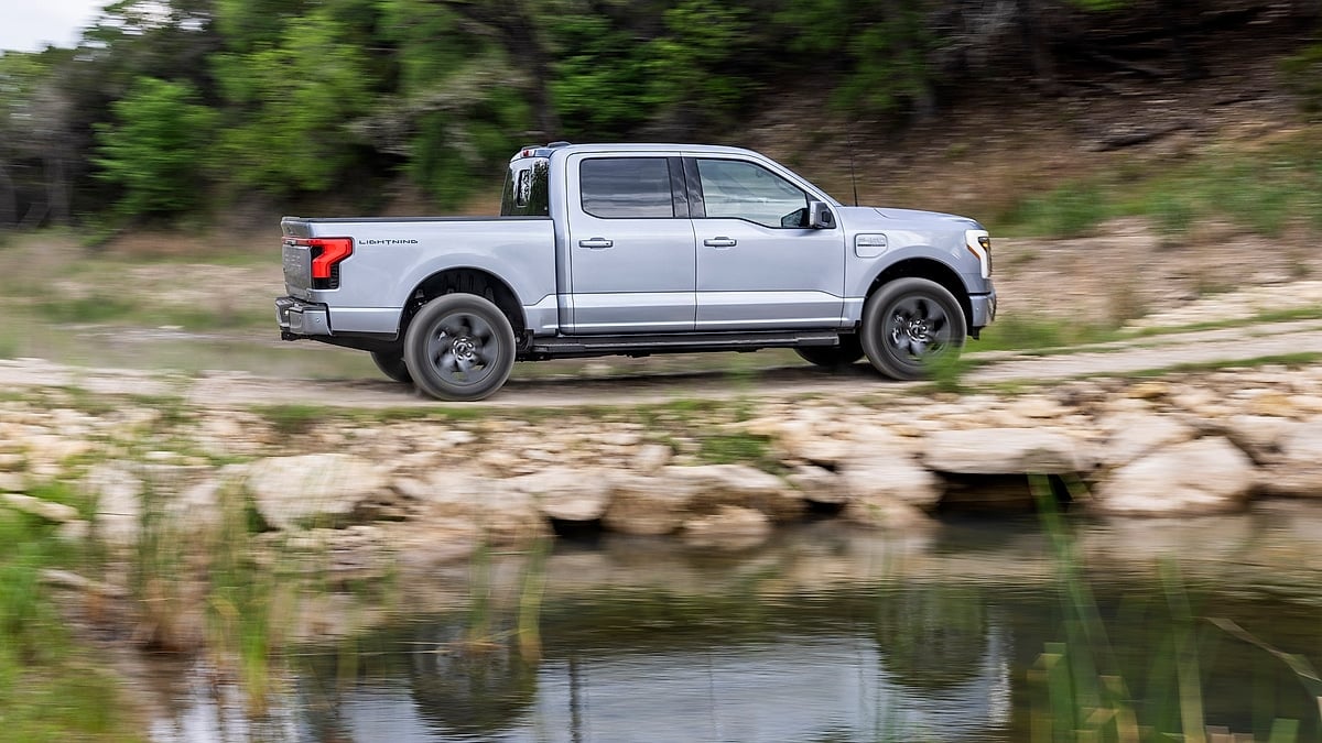 Silver Ford F-150 Lightning Lariat driving off-road beside a creek in a side-profile action view.