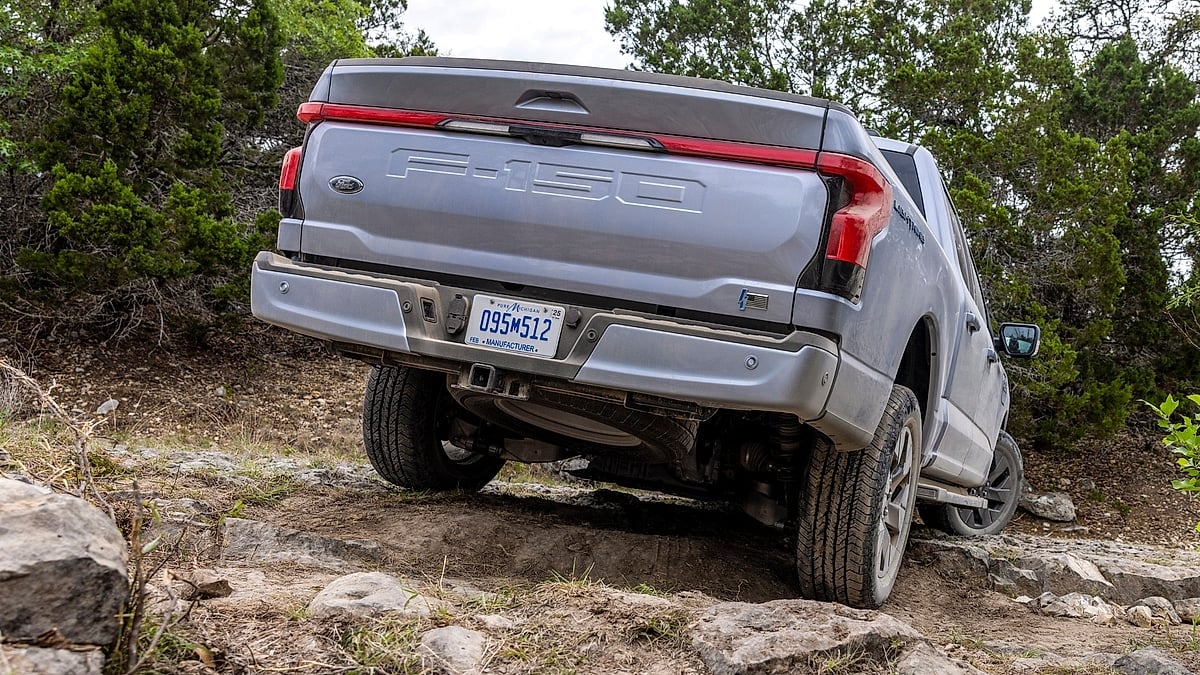 Silver Ford F-150 Lightning Lariat driving over rocks on an off-road trail in a rear three-quarter view.