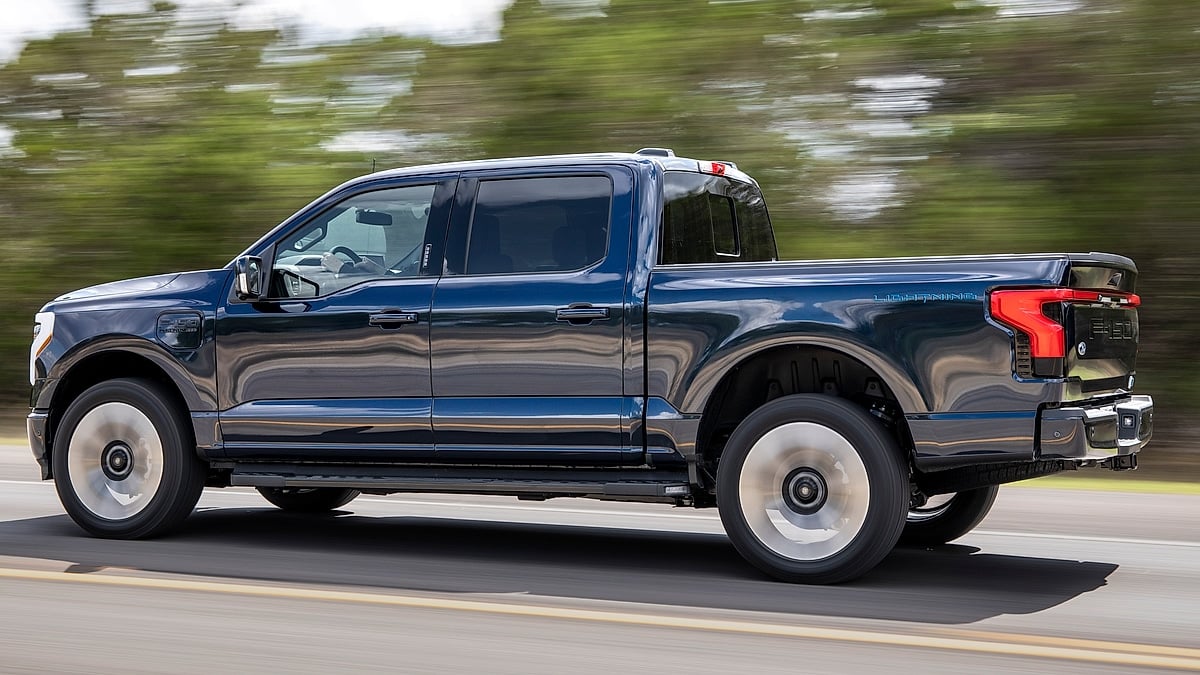 Blue Ford F-150 Lightning Platinum driving on a road in a side-profile action view.