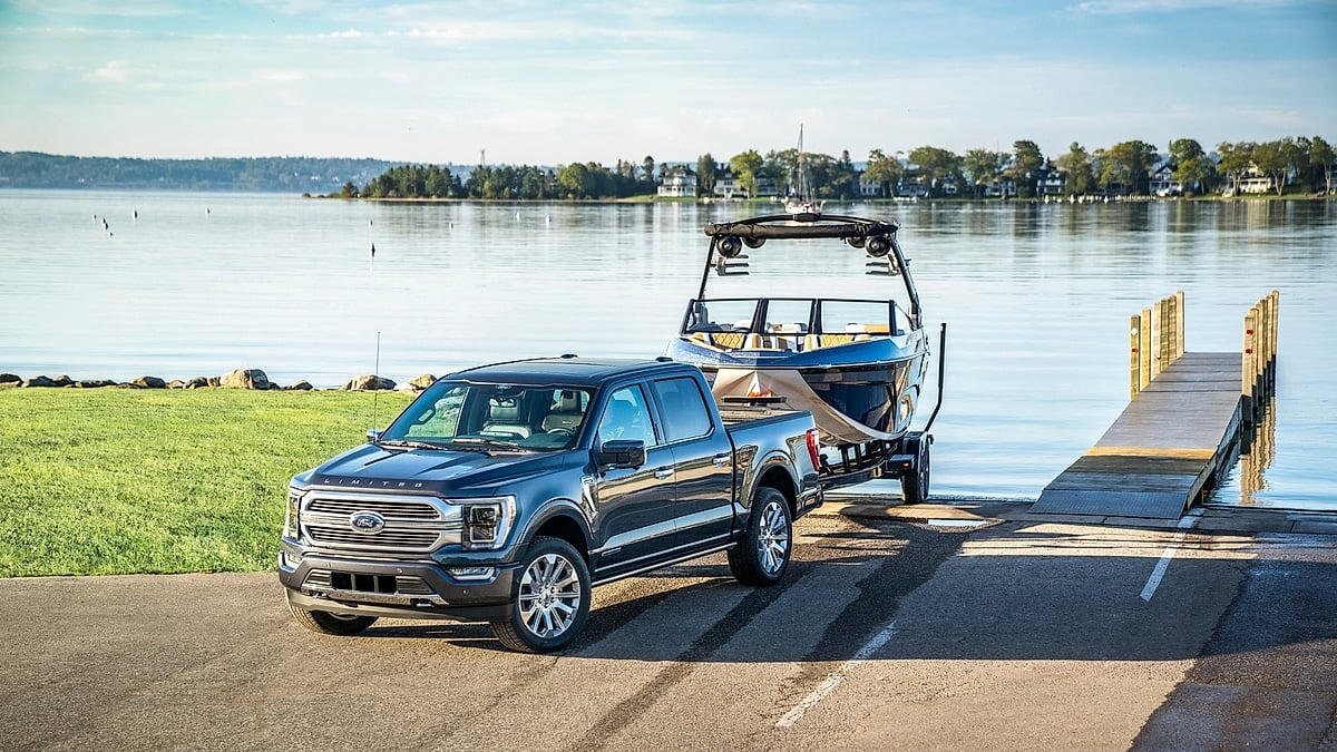 Ford F-150 Limited towing a boat on a trailer near a lakeside boat ramp.