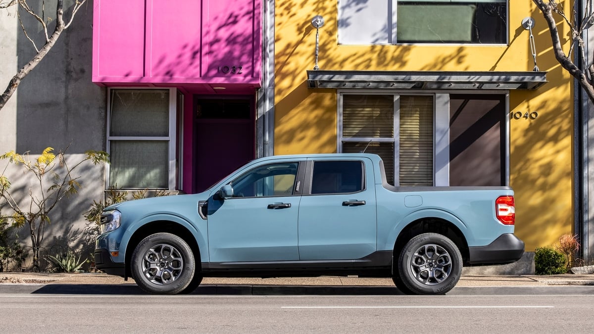 Light blue Ford Maverick XLT pickup truck parked on a city street lined with colorful green, pink, and yellow building facades